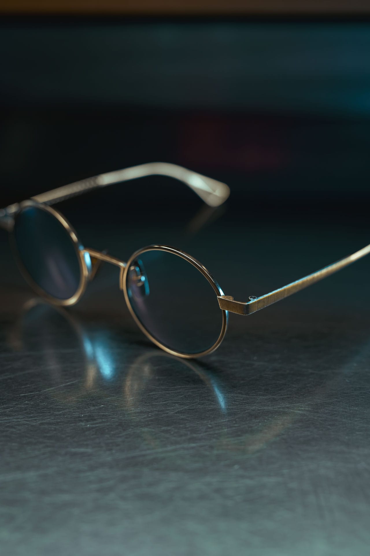 A pair of round gold eyeglasses on a steel surface