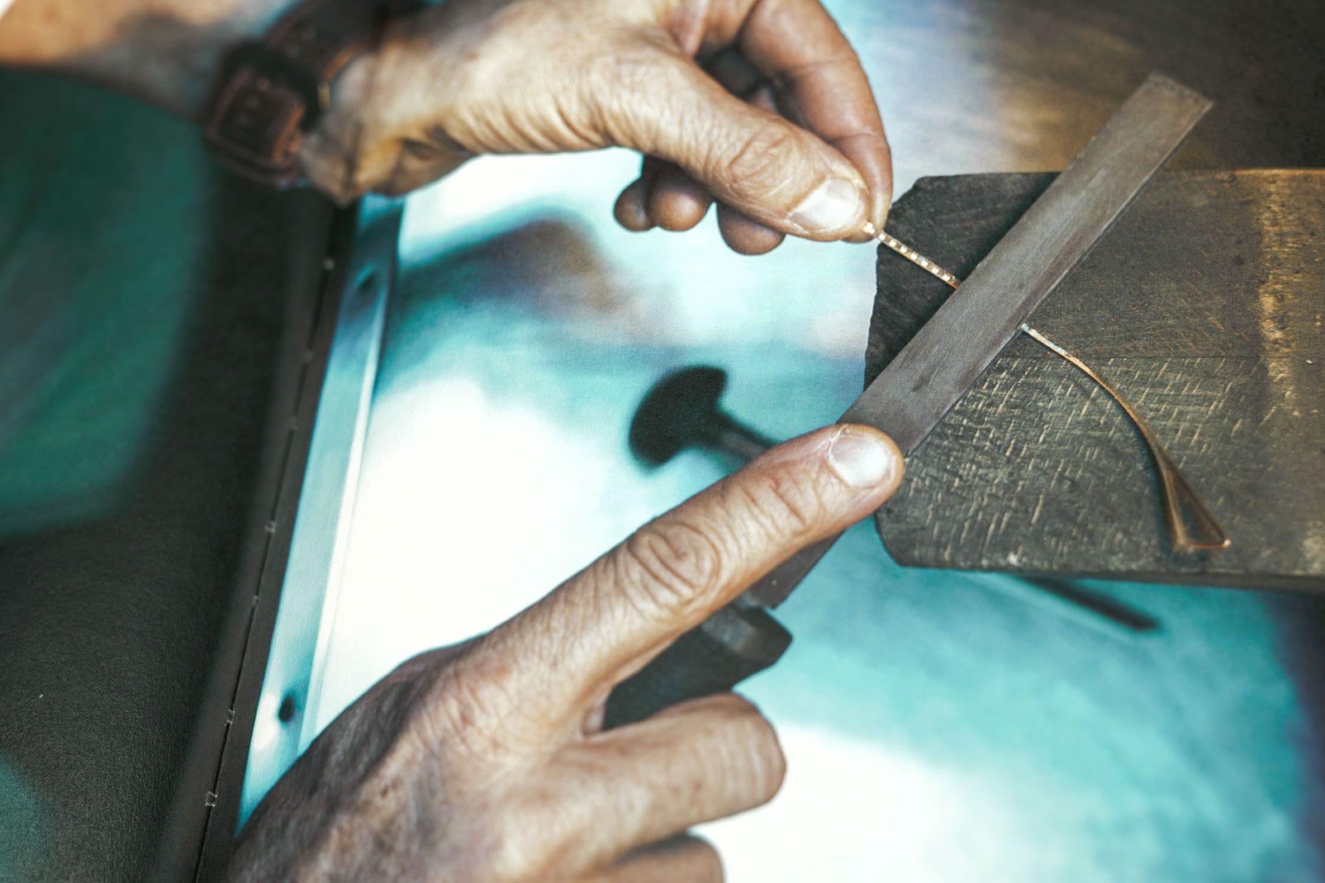 Hands filing a gold eyeglass frame at a workbench