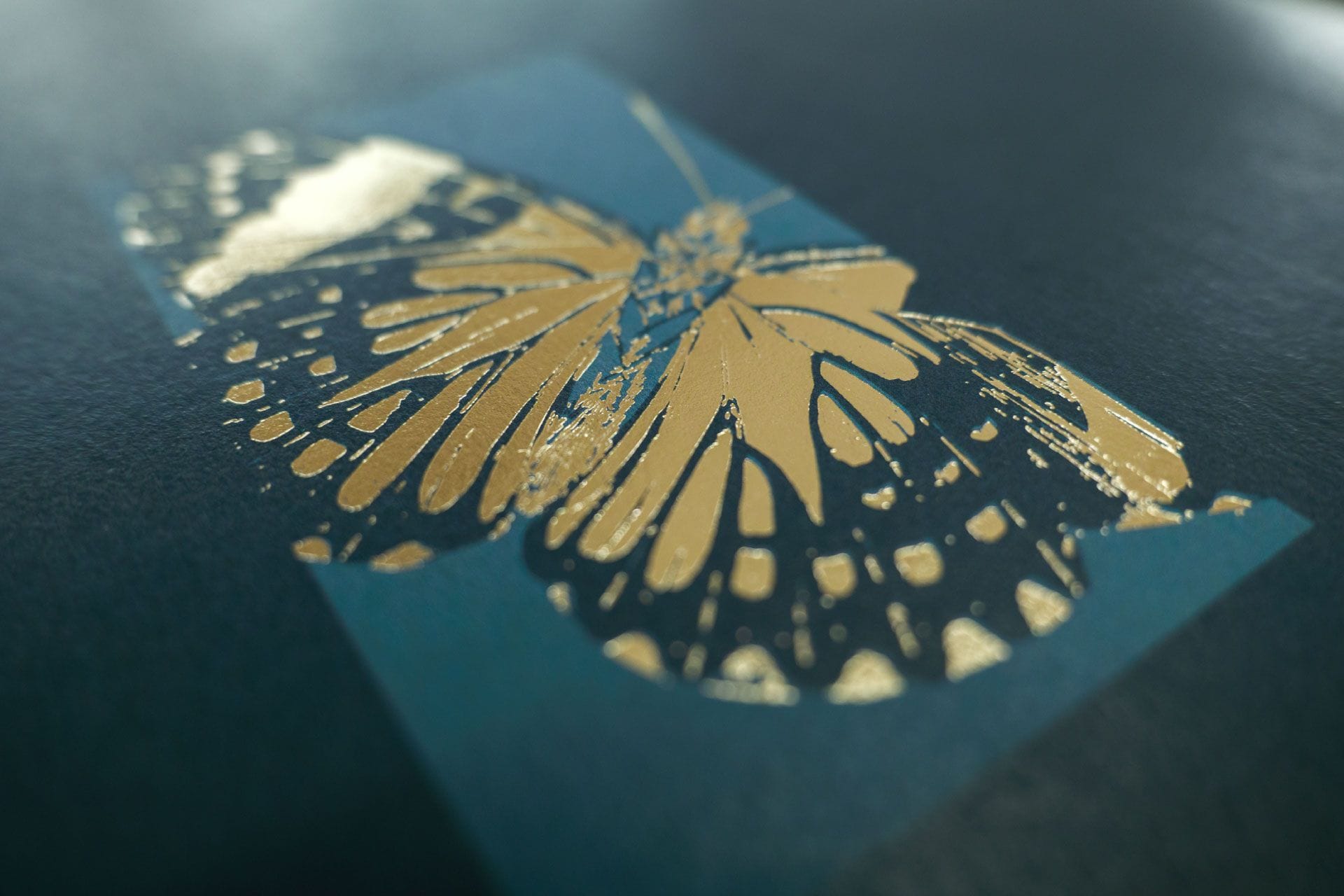 A butterfly illustration in gold foil on blue paper